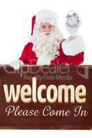 Composite image of santa claus holding alarm clock and sign