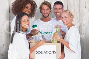 Composite image of happy volunteers putting food in donation box