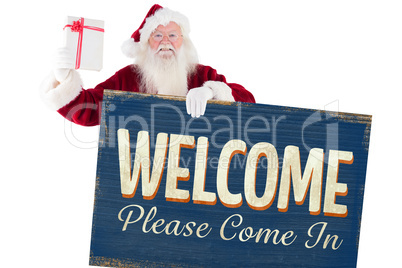 Composite image of santa shows a present while holding sign