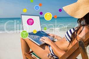 Composite image of pretty brunette using laptop on deck chair