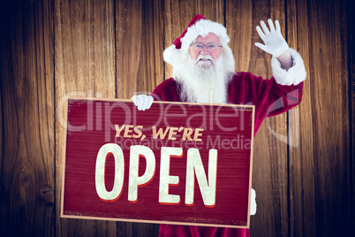 Composite image of santa holds a sign and is waving