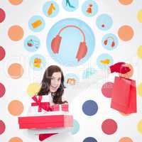 Composite image of excited brunette holding gifts and showing sh
