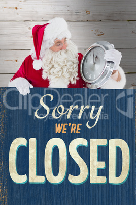 Composite image of santa holding a clock and sign