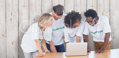 Composite image of smiling volunteers working together on a lapt