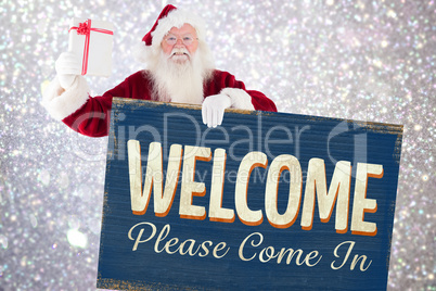 Composite image of santa shows a present while holding sign