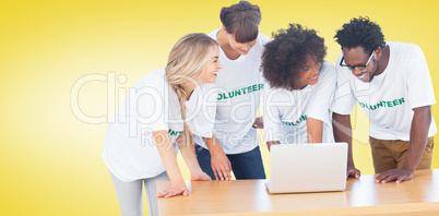 Composite image of smiling volunteers working together on a lapt