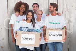 Composite image of happy group of volunteers holding clothes don