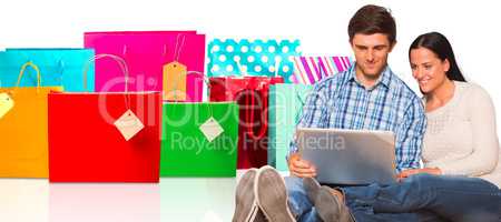 Composite image of young couple sitting on floor with laptop