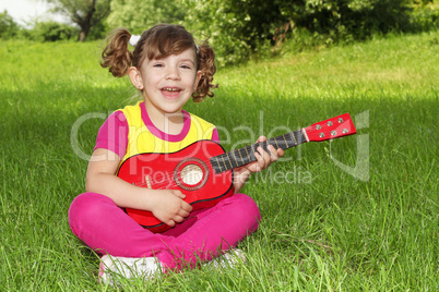 little girl sitting on grass play guitar and sing