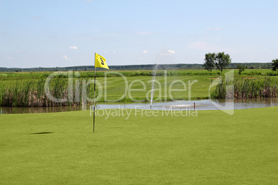 golf field with yellow flag and pond