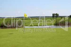 golf field with yellow flag and pond