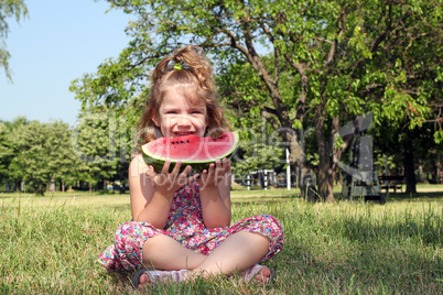 little girl sitting on grass and eat watermelon