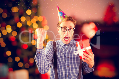 Composite image of geeky hipster wearing party hat holding gift