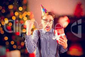 Composite image of geeky hipster wearing party hat holding gift