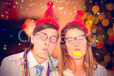 Composite image of geeky hipster wearing a party hat with blowin