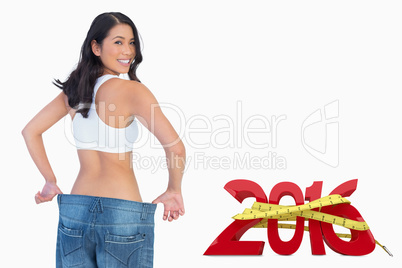 Composite image of woman holding her too big jeans smiling