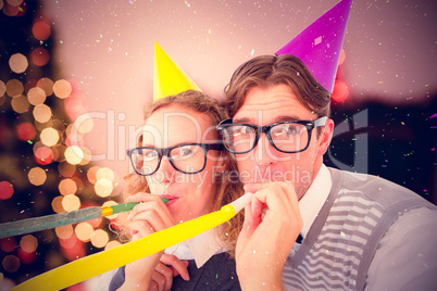 Composite image of geeky hipster couple blowing party horn
