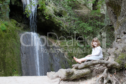 little girl sitting next to a waterfall