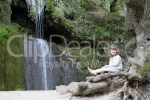 little girl sitting next to a waterfall