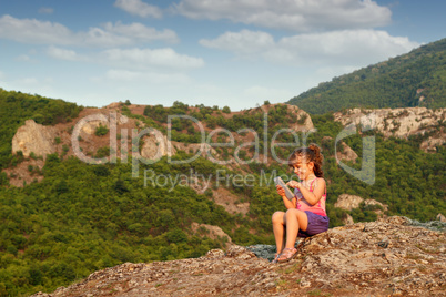 little girl sitting on a mountain top and play with tablet