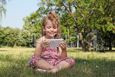 little girl sitting in park and play with tablet pc