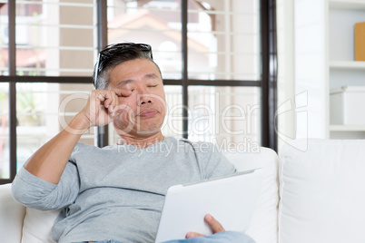 Mature Asian man eyes pain while using tablet computer