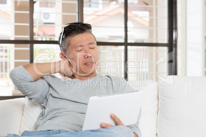 Mature Asian man neck pain while using tablet computer