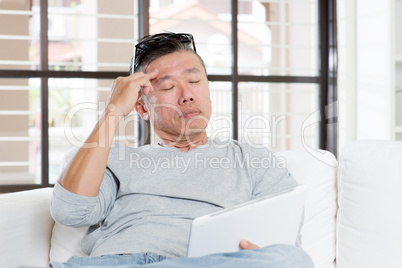 Mature Asian man headache while using tablet computer