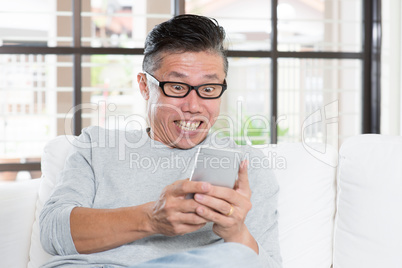 Mature Asian man getting excited while using smartphone