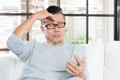 Mature Asian man headache while using smartphone
