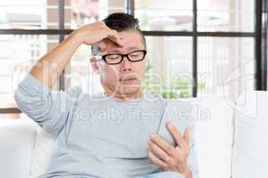 Mature Asian man headache while using smartphone