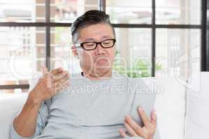 Mature Asian man unhappy while using smartphone