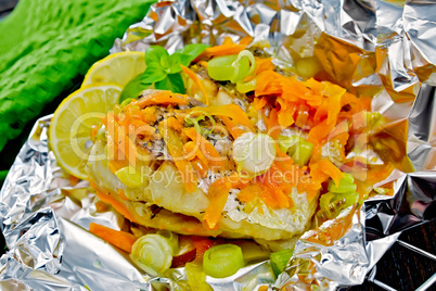 Pike with carrots and leeks in foil on dark board