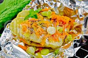 Pike with carrots and leeks in foil on dark board