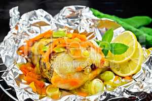 Pike with carrots and onions in foil on dark board