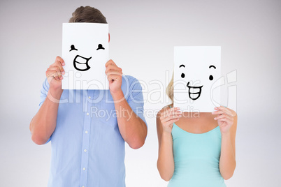 Composite image of young couple holding pages over their faces
