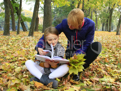 mother and daughter read a book in the autumn park