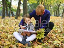 mother and daughter read a book in the autumn park