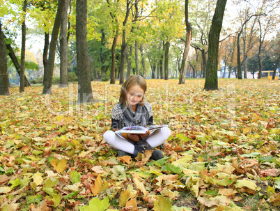 young girl reads a book in the autumn park