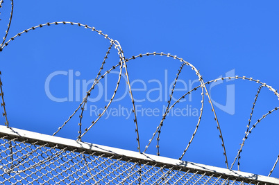 Fence with a barbed wire against the blue sky.
