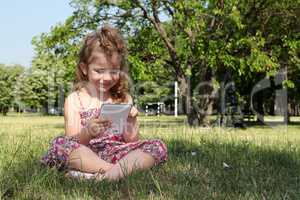 little girl sitting on grass and play with tablet pc