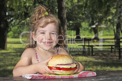 little girl with big sandwich sitting in park