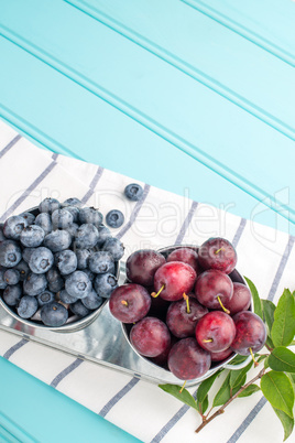 Plums and blueberries in small metal bucket