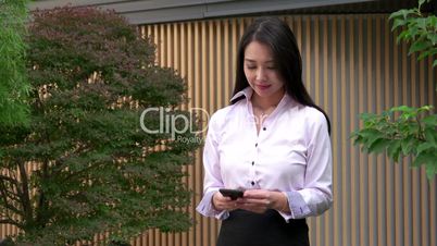 Young Asian Woman Texting Message With Smartphone Near Office Smiling