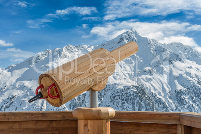 Aussichtspunkt mit Fernrohr aus Holz mit verschneiter Berglandschaft im Hintergrund