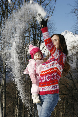 Happy mother holding her daughter in her arms in the winter woods on a sunny day