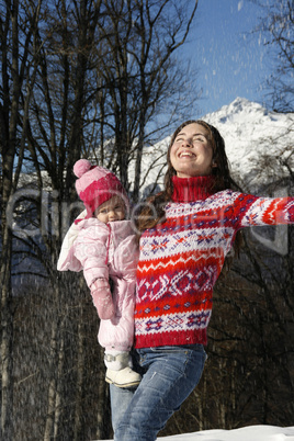 Happy mother holding her daughter in her arms in a forest in winter