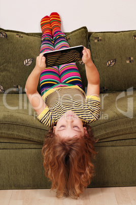 little girl lying upside down on bed and play with tablet