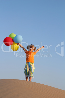 happy little girl with balloons standing on sand dune