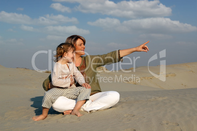 happy mother and daughter sitting on sand family scene